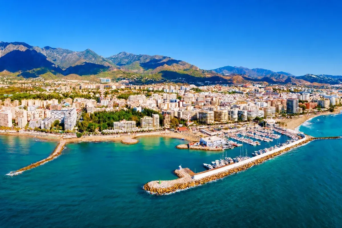 Aerial view of a Costa del Sol city, marina and beach backed by mountains