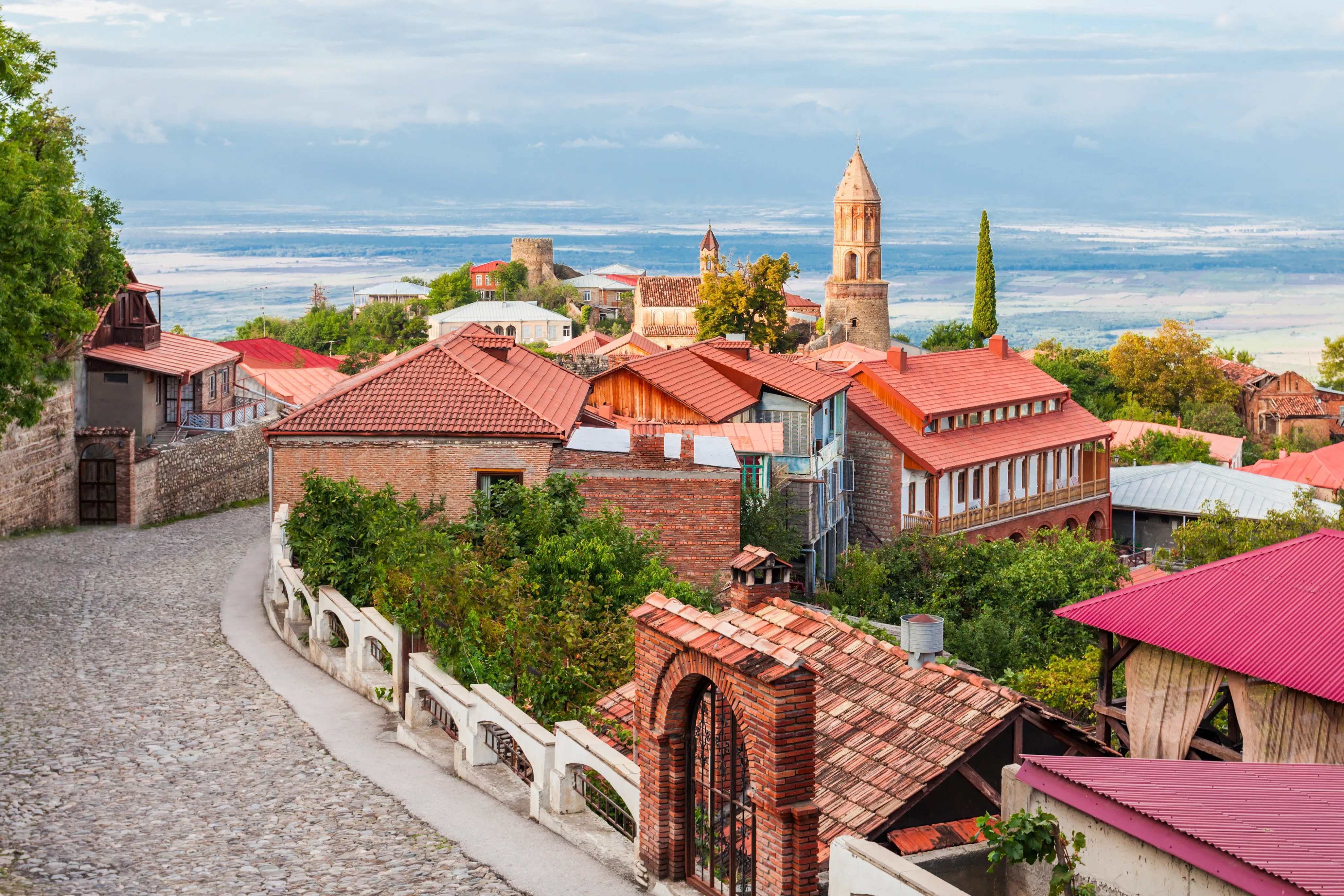 Historic hillside town in Georgia with red-roofed houses, stone streets, a church tower, and a broad valley in the distance.