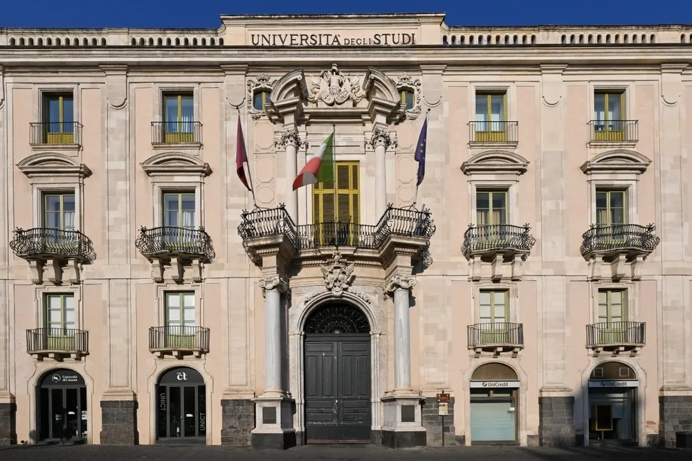 Historic university building in Piazza Università, Italy, featuring an ornate entrance, balconies and the Italian flag.