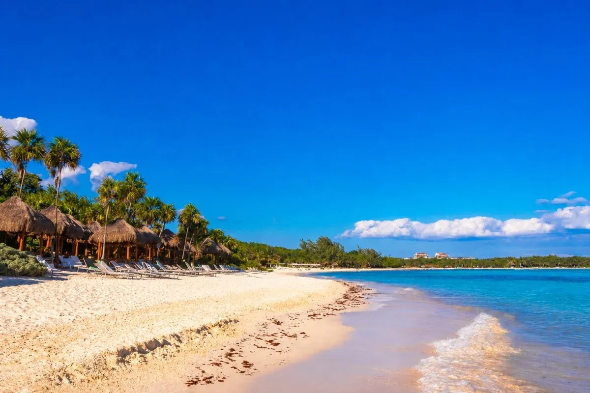 Palapa huts and lounge chairs on a white-sand beach in Playa del Carmen, Mexico