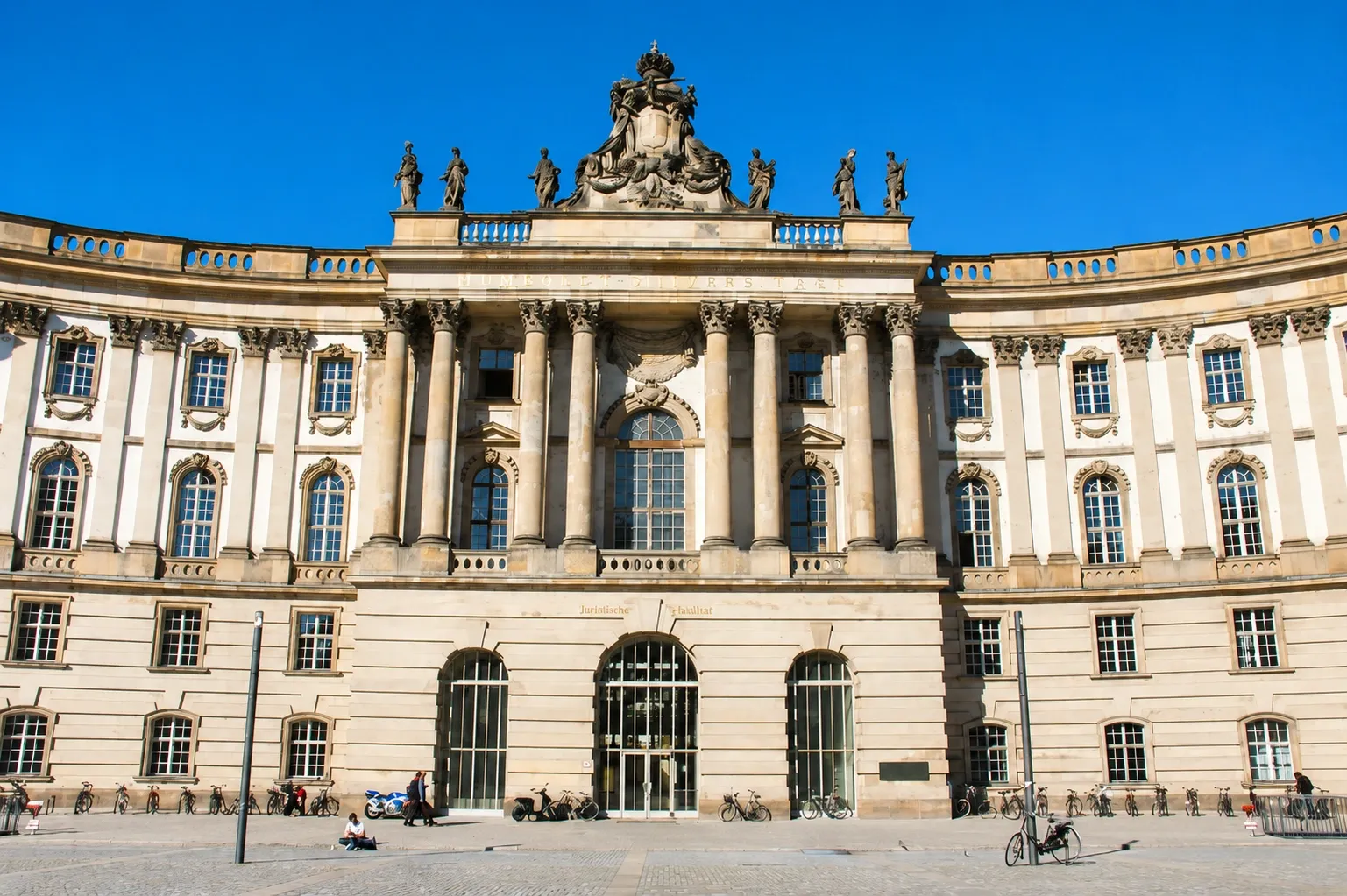 Historic Humboldt University building in Berlin with classical columns, ornate architecture and a bright blue sky.