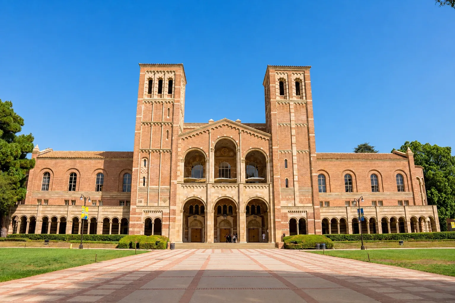 Grand red-brick University of California campus building with twin towers, arched entrances and a clear blue sky.