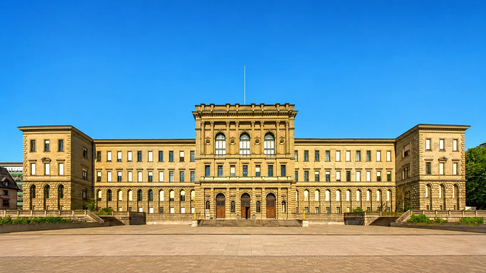 Grand historic university building in Zurich with a symmetrical stone façade, large courtyard and clear blue sky.