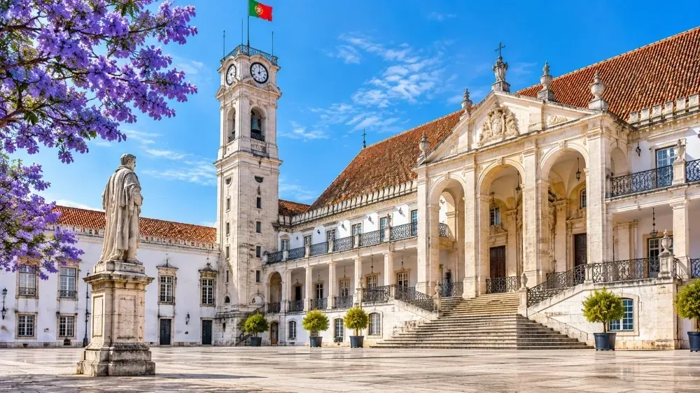 Historic Portuguese university courtyard with a clock tower, grand staircase, classical architecture and Portugal’s flag.